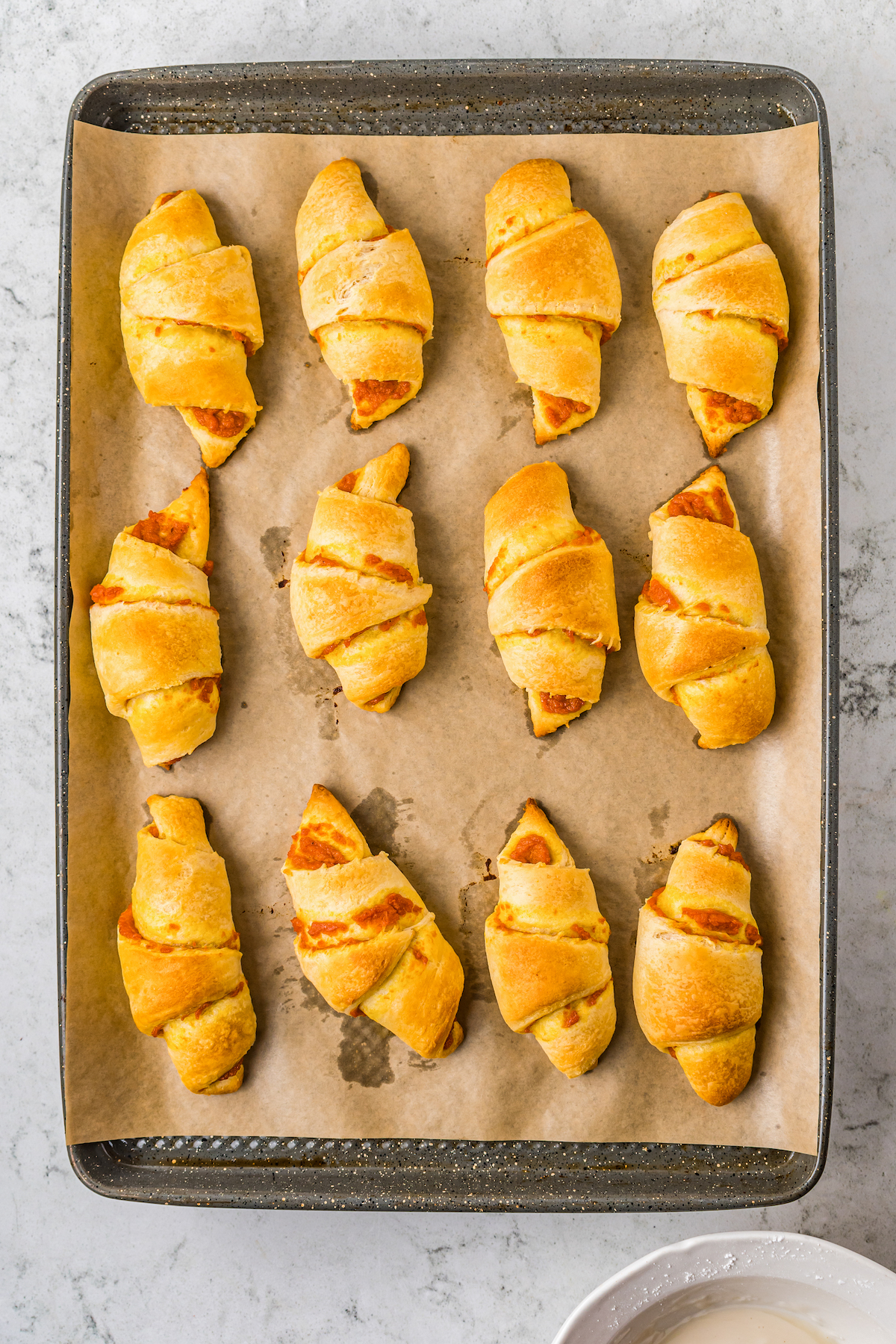 Crescent rolls lined up on a baking sheet with a crispy golden outside and filling showing through.
