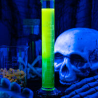 a glowing shot of liquor in a tall graduated cylinder with a skull next to it