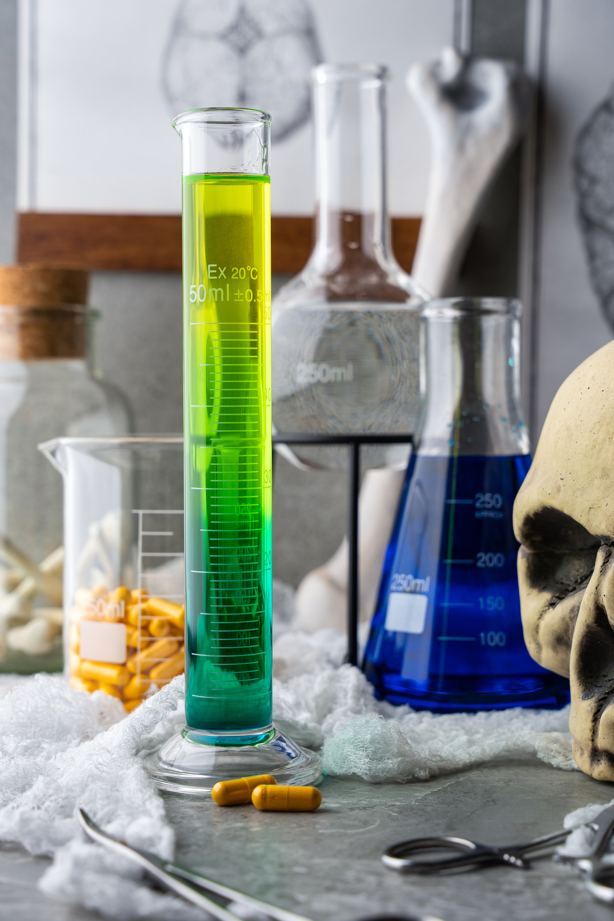 a shot of liquor that gradually turn from green to yellow in a tall graduated cylinder on a table with Halloween decorations