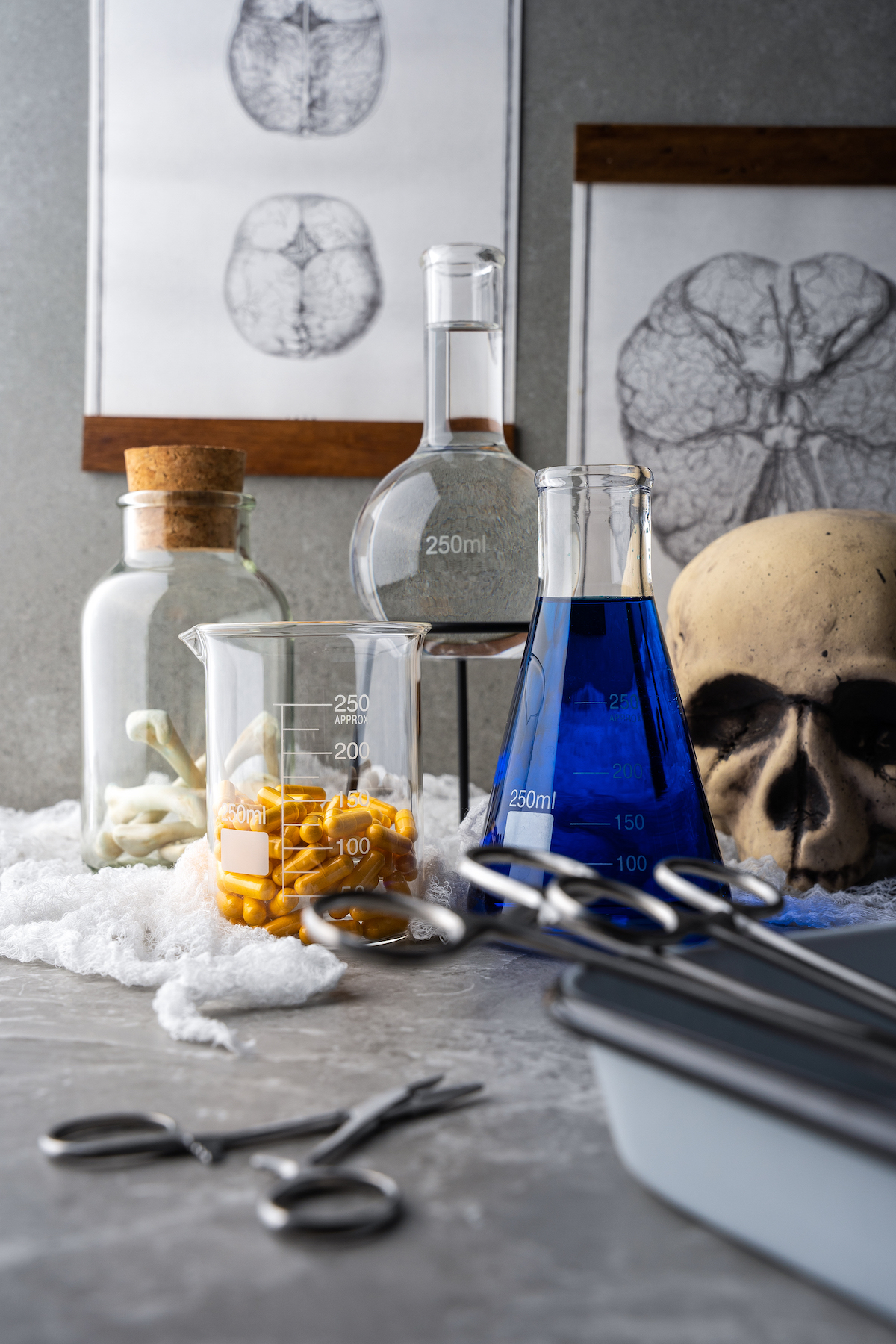 a mad scientist themed tablescape with various measuring glasses, scirrors, a glass pitcher with pills, and a blue potion