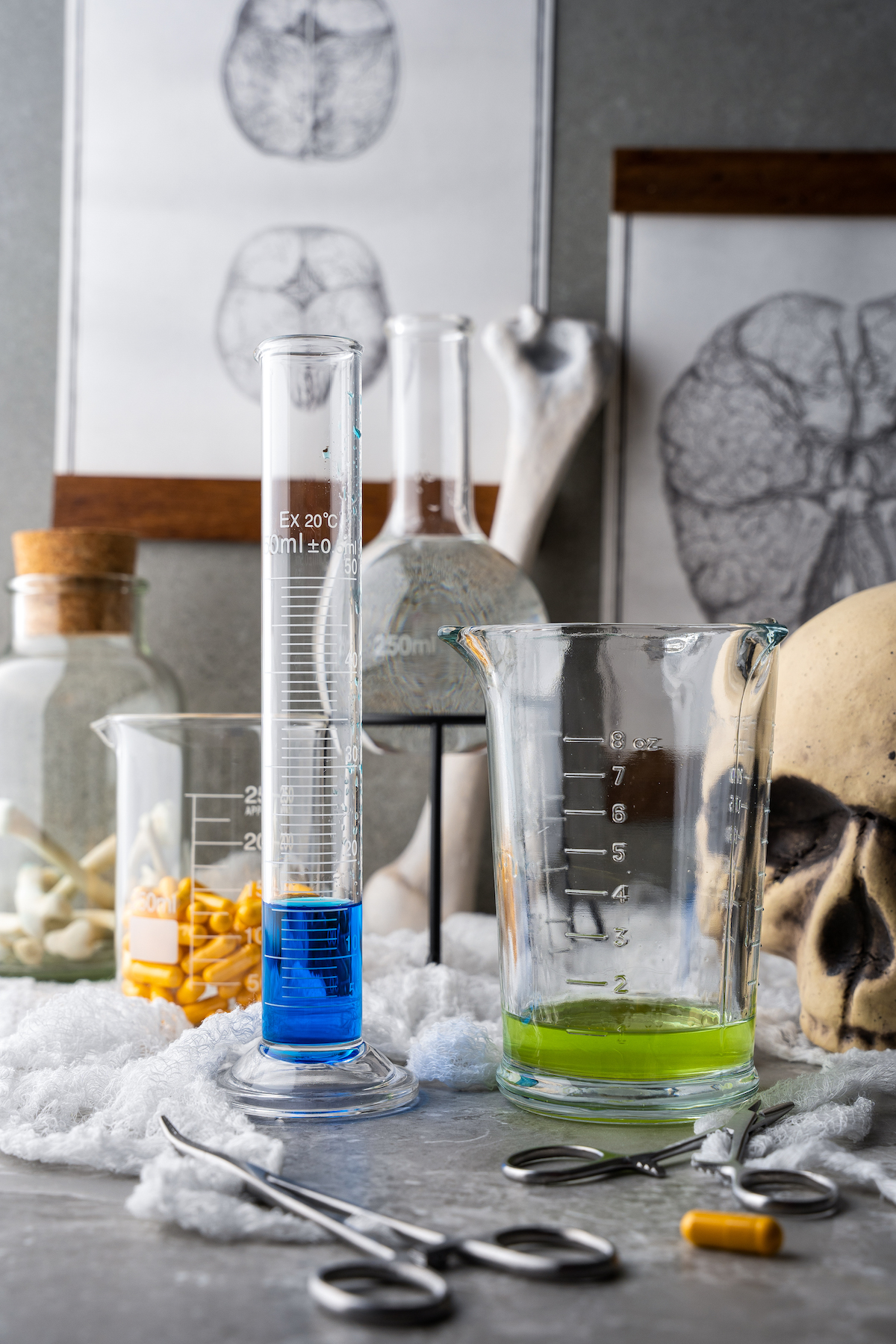 a tall graduated cylinder with blue curacao on a tablescape with other mad scientist themed Halloween decorations