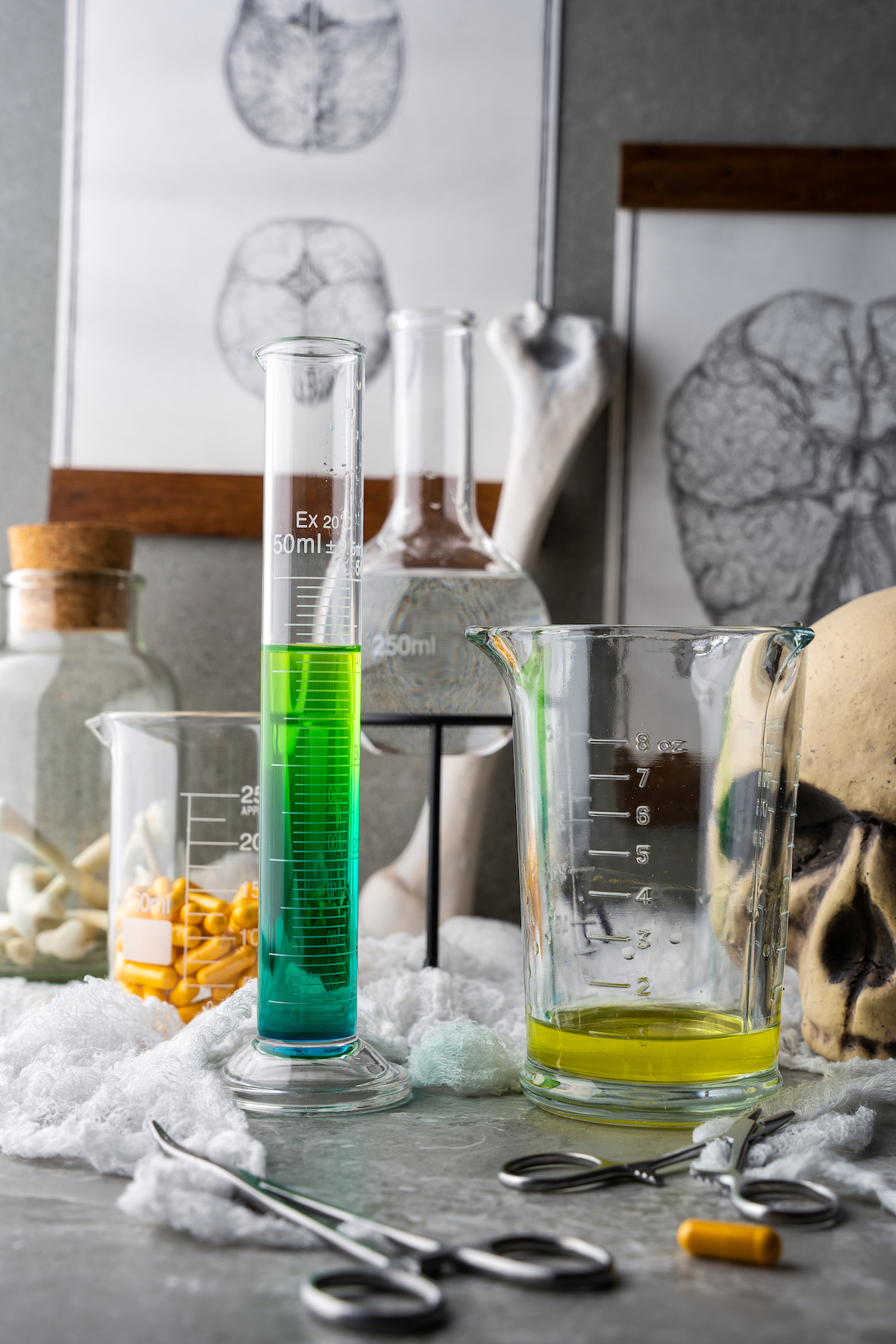 a shot of liquor that gradually turns from blue to green in a tall graduated cylinder on a table with Halloween decorations