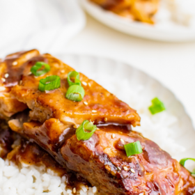 Teriyaki Salmon over rice on a white plate with green onions.