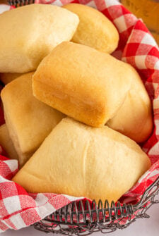 Square dinner rolls in a basket lined with a red and white checked cloth napkin.