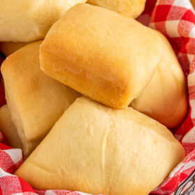 Square dinner rolls in a basket lined with a red and white checked cloth napkin.