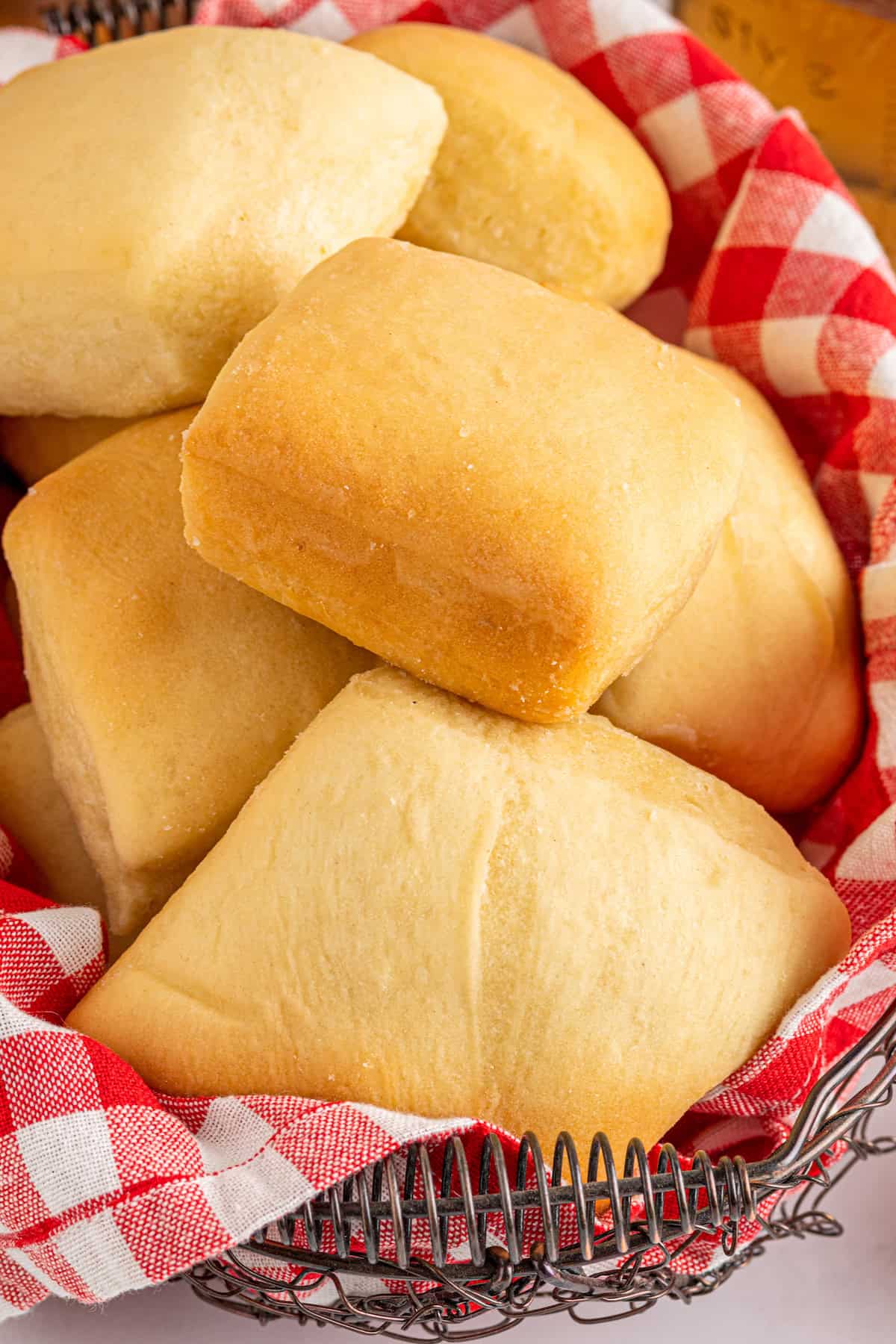 Soft, square copycat Texas Roadhouse rolls arranged in a basket lined with a red and white checked cloth napkin.