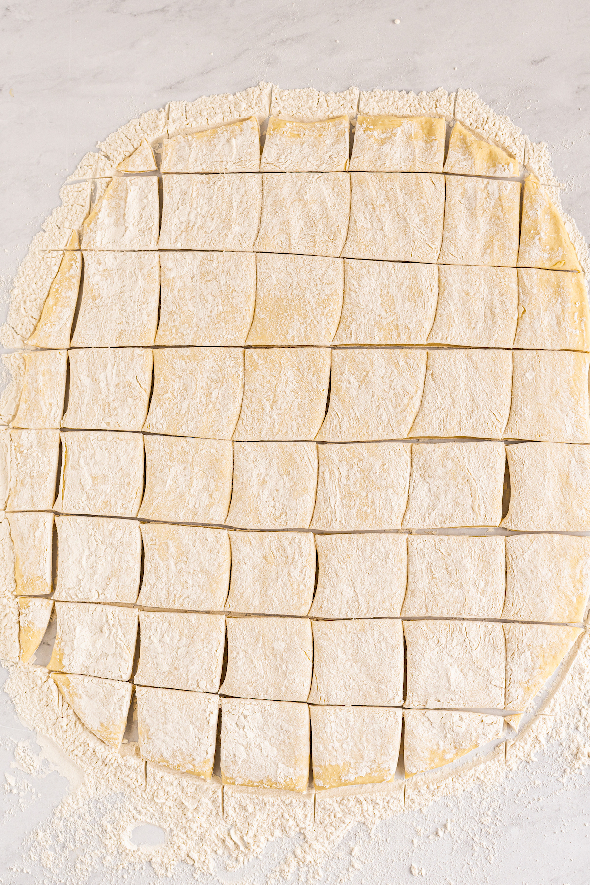 Dough, rolled out and cut into squares, on a work surface.
