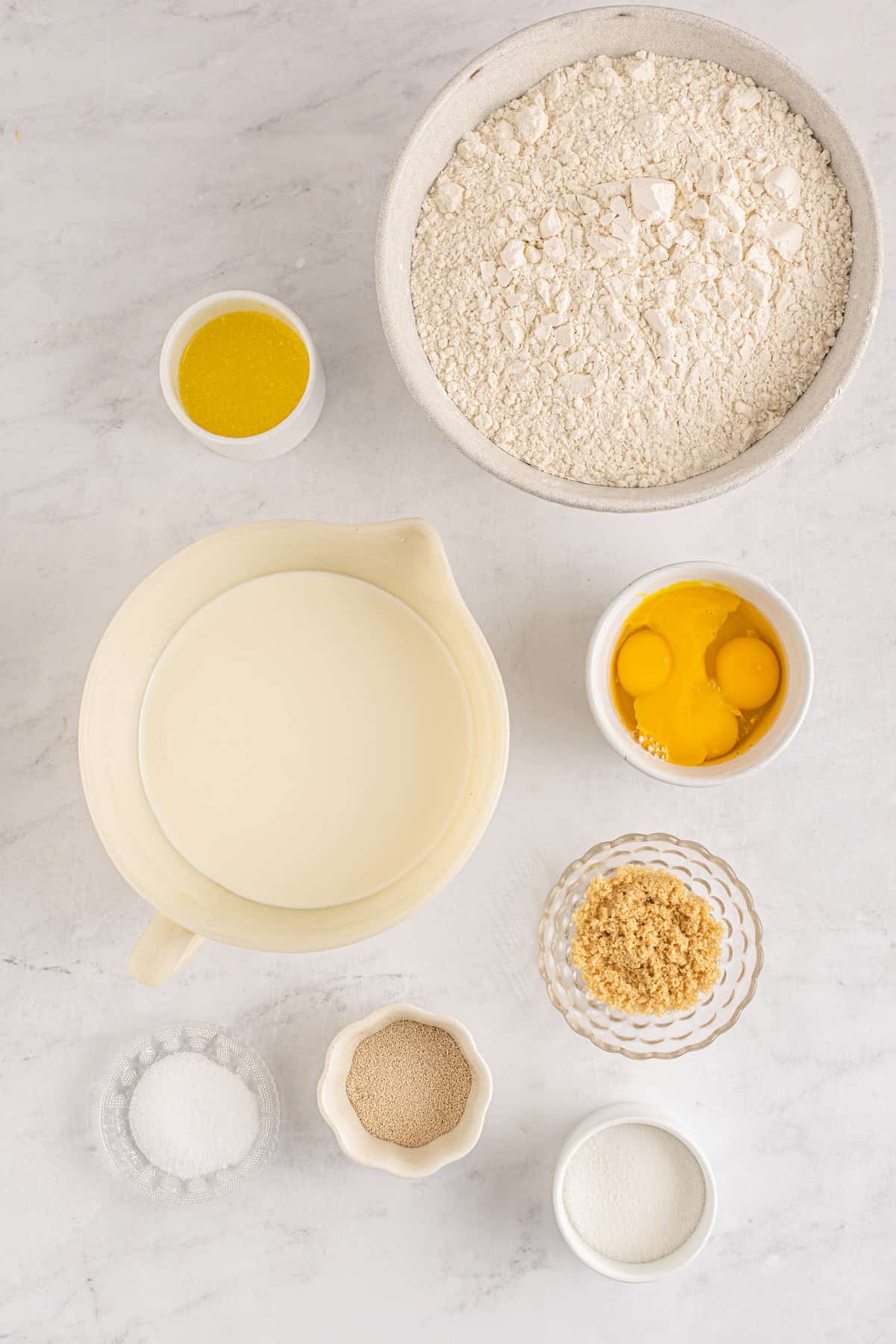 Ingredients needed for copycat Texas Roadhouse rolls recipe arranged in bowls. From top let: Melted butter, flour, milk, eggs and egg yolks, sugar, yeast, brown sugar.