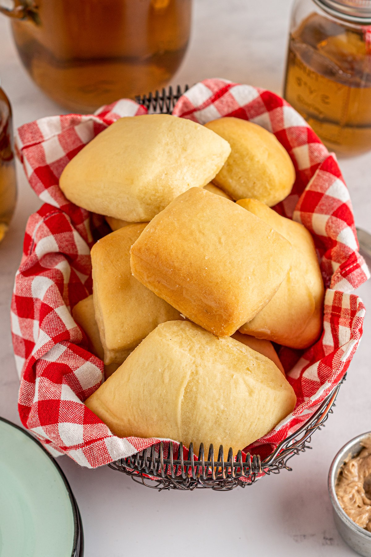 Soft and warm copycat Texas Roadhouse rolls fresh out of the oven stacked on top of each other in a basket lined with a red and white checkered napkin.