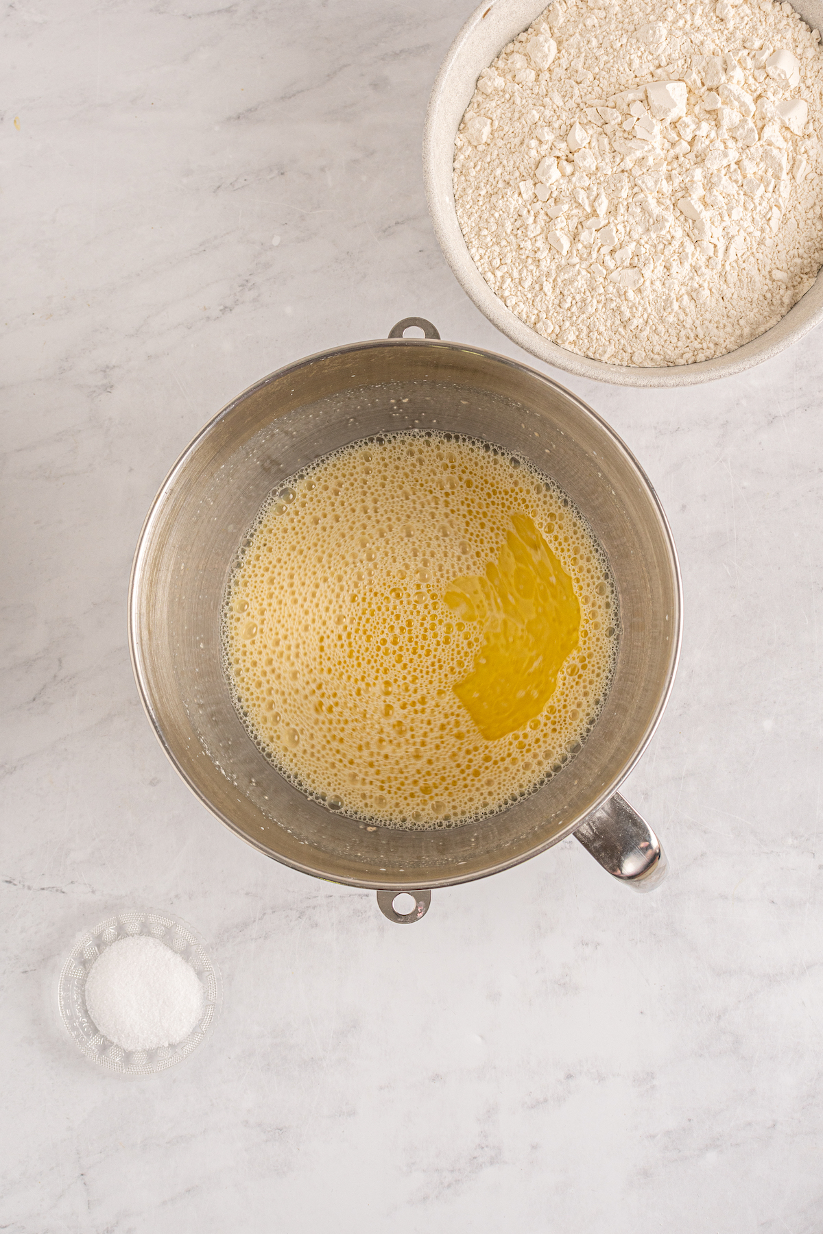 Melted butter, eggs, yeast, and other dinner roll ingredients in a metal mixing bowl.