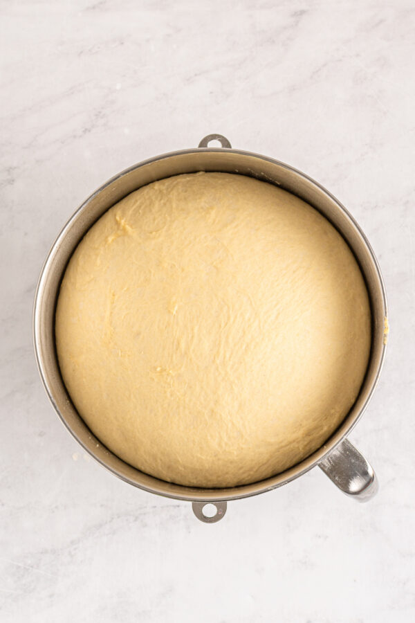 Risen dough in a metal mixing bowl.