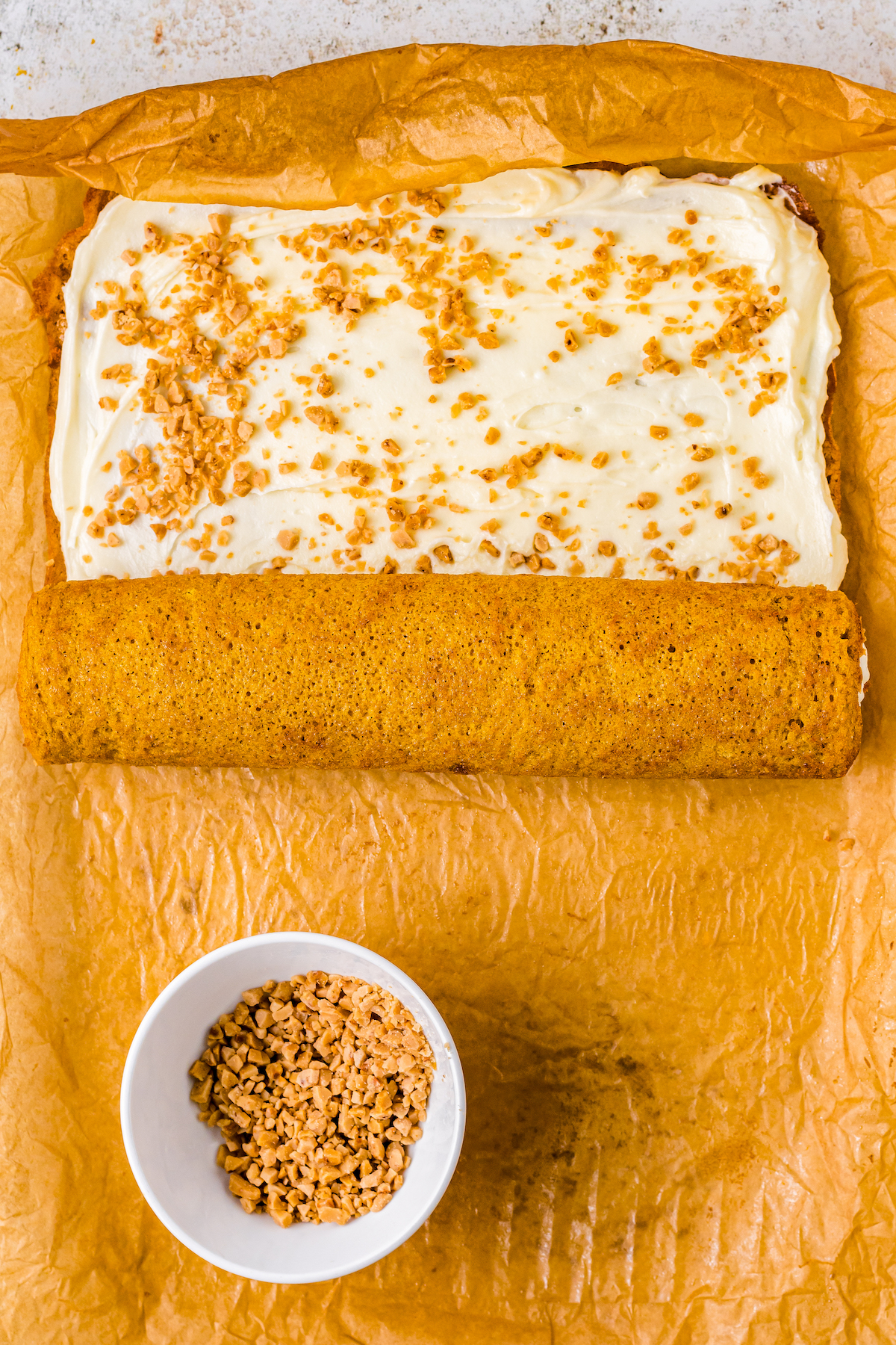 A pumpkin roll cake being rolled up around creamy filling and toffee bits.
