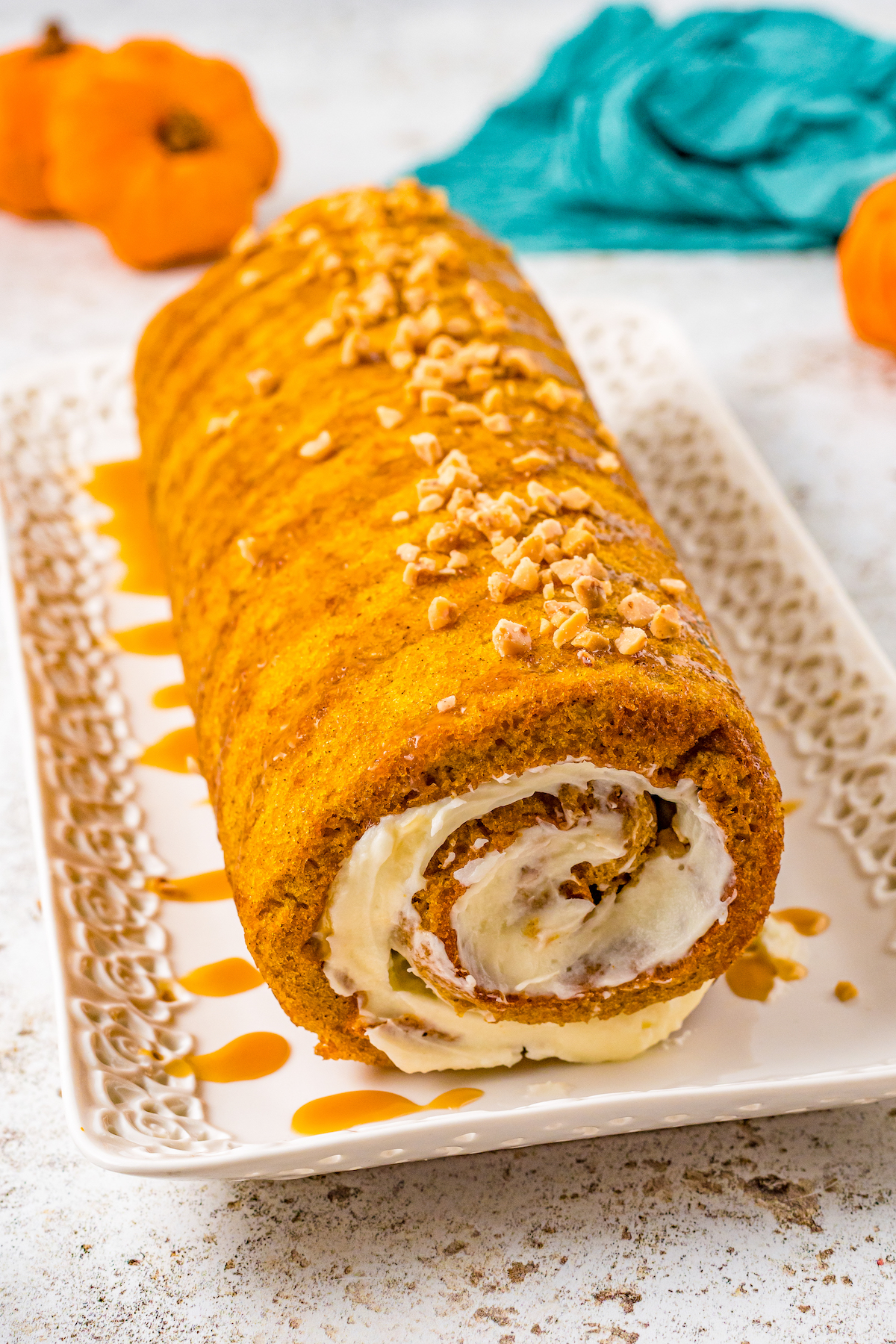 Front view of a pumpkin roll on a rectangular plate, drizzled with caramel and sprinkled with toffee.