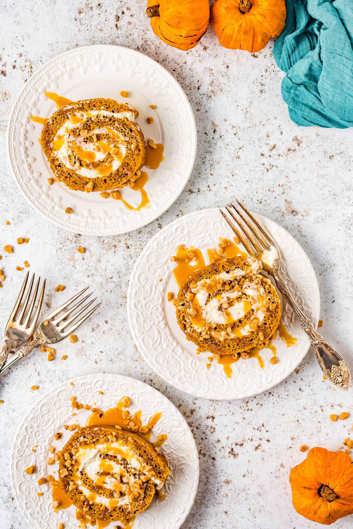 Servings of pumpkin spice jelly roll on dessert plates, garnished with caramel drizzle and toffee bits.