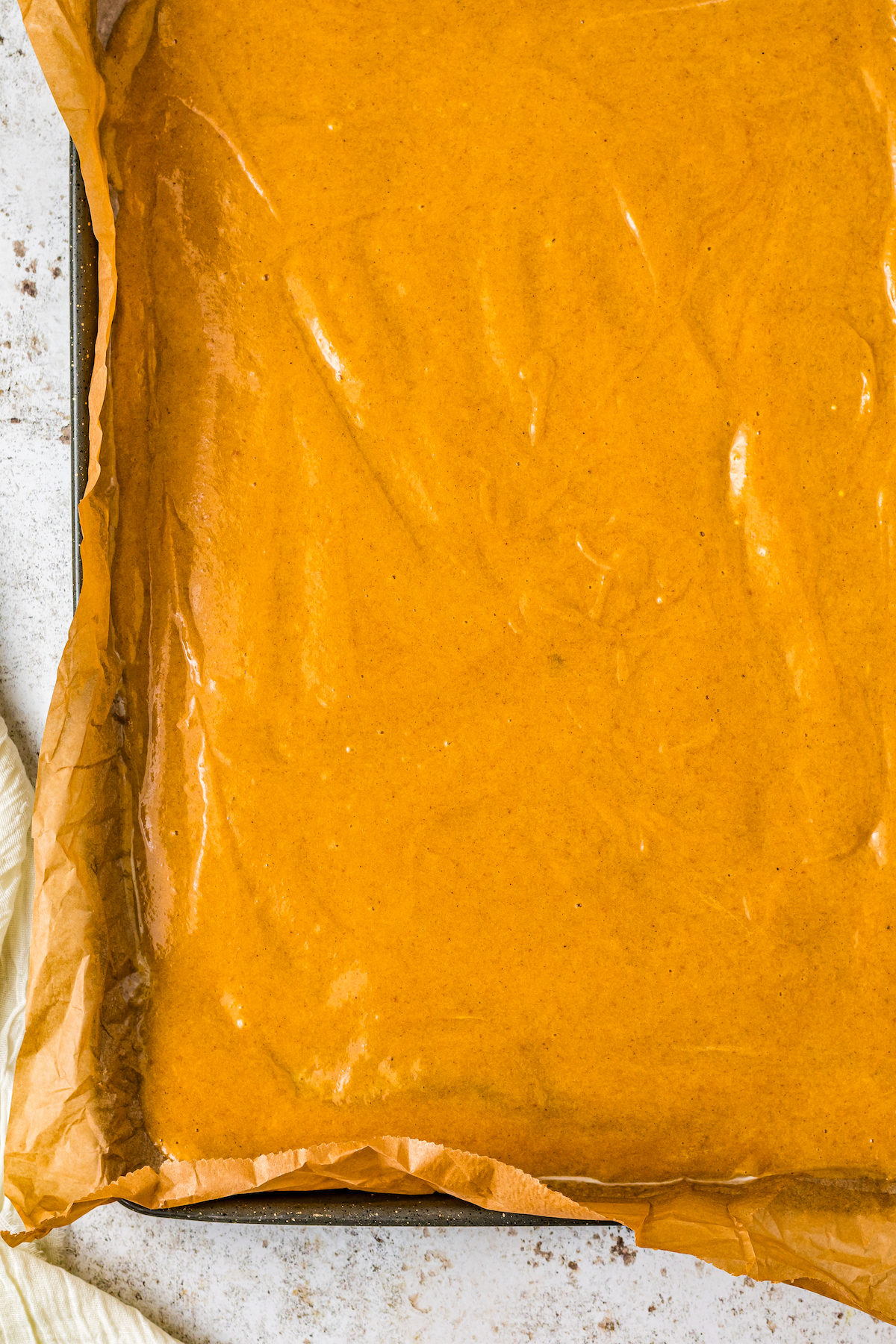 A parchment-lined jelly roll pan, filled with unbaked pumpkin batter.