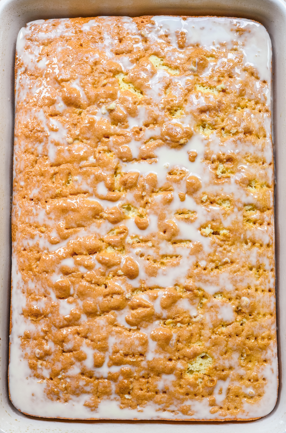 A perforated vanilla cake layer with a three milk mixture poured over the top.