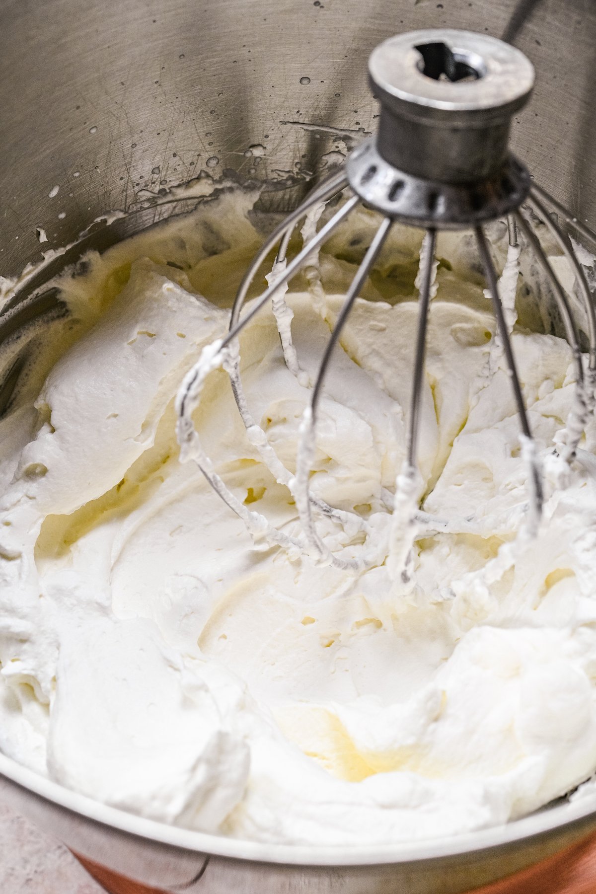 Heavy cream whipped into stiff peaks in a mixing bowl with the whisk mixer attachment inside.