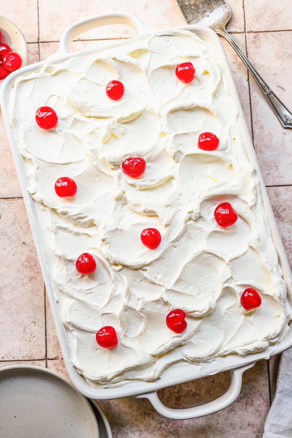 A pan full of Tres Leches Cake seen from above dotted with maraschino cherries.