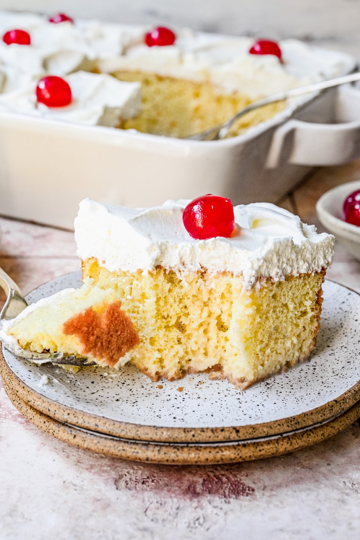 Tres Leches Cake on a plate with a single bite taken out of it and balanced on a fork next to it.
