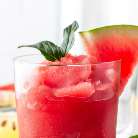 A glass of watermelon frosé with a watermelon wedge and fresh basil on top.