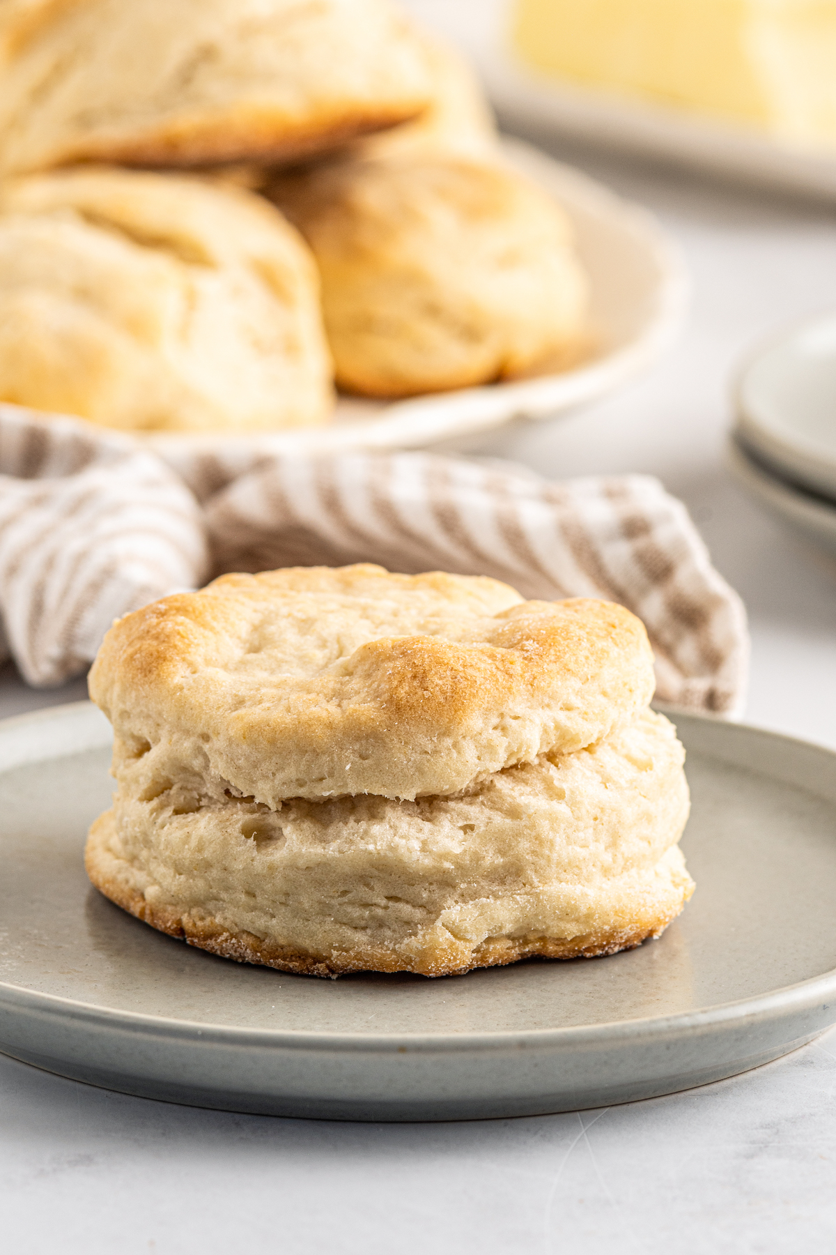 A 7-Up biscuit on a small plate, with a platter of biscuits in the background of the shot.