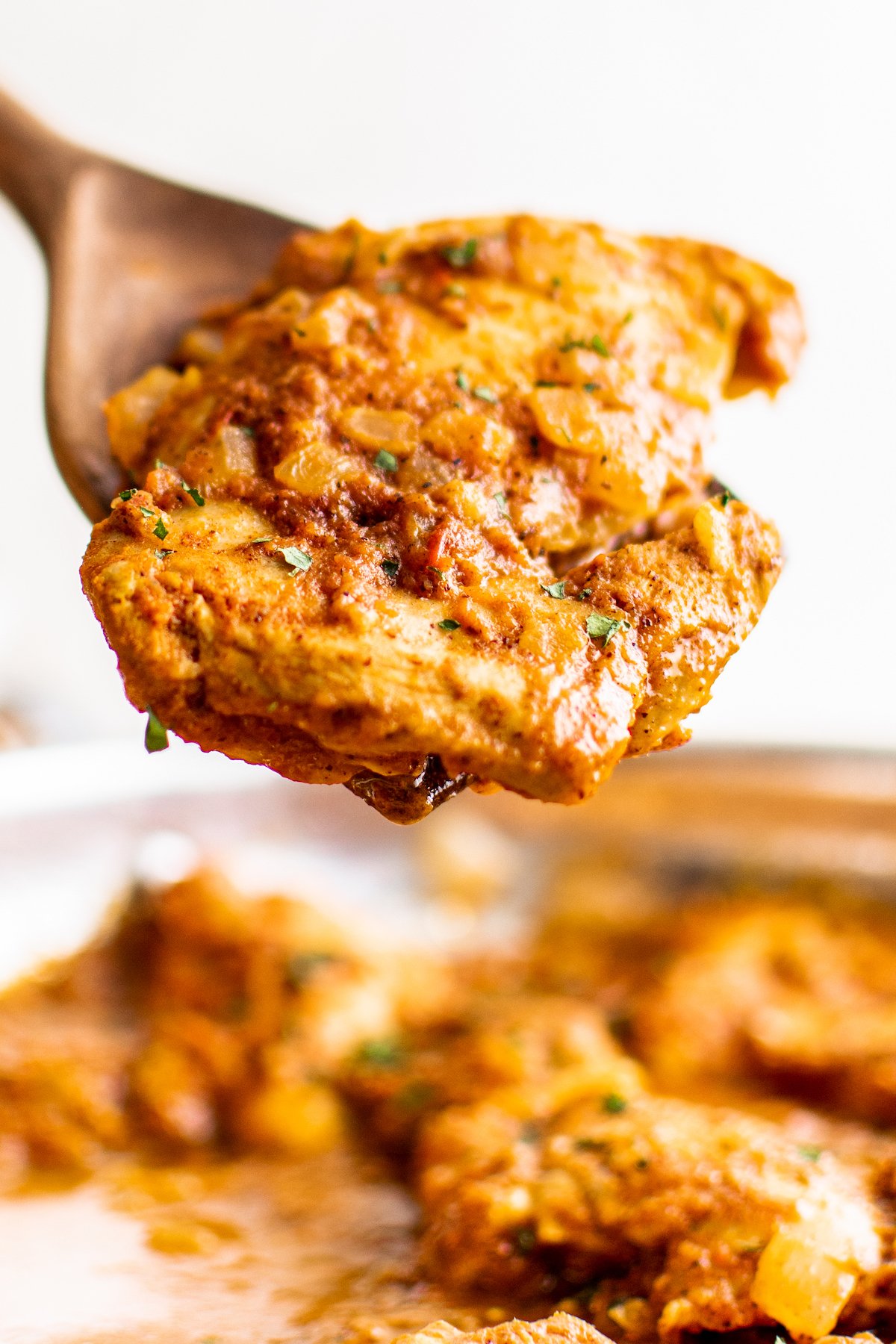 A piece of achiote chicken being taken out of a pan with a wooden spoon