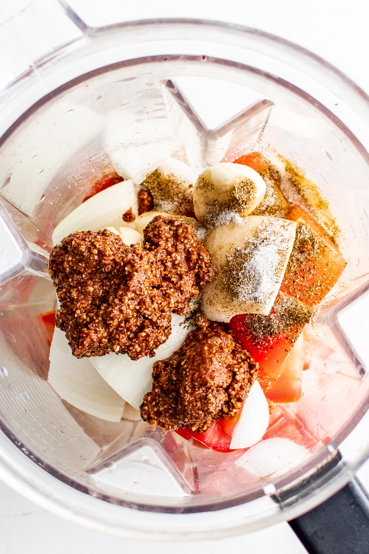 A blender filled with onions, garlic, tomatoes, and achiote paste