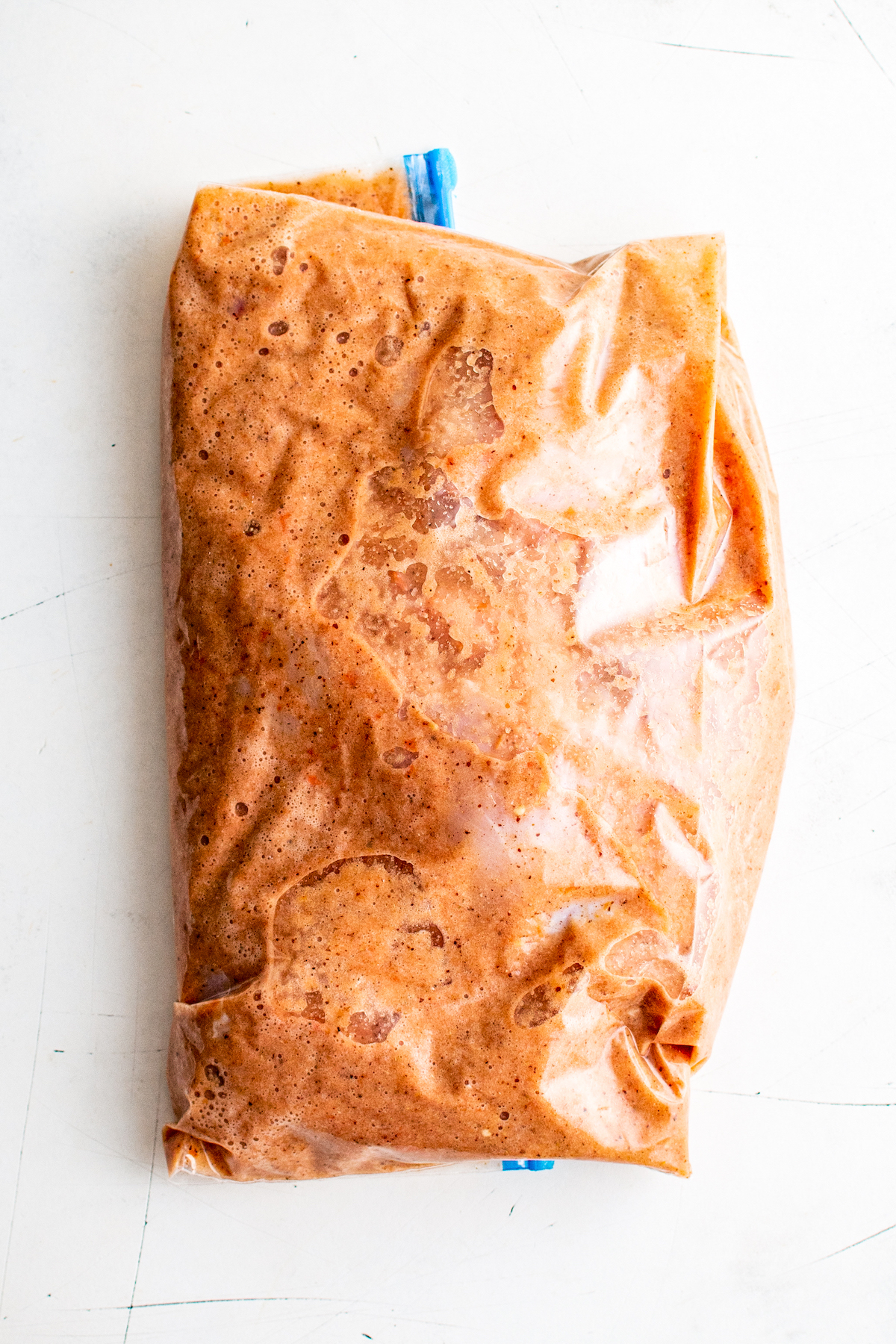 A ziploc bag with raw chicken and achiote marinade in it, sealed with the air pressed out
