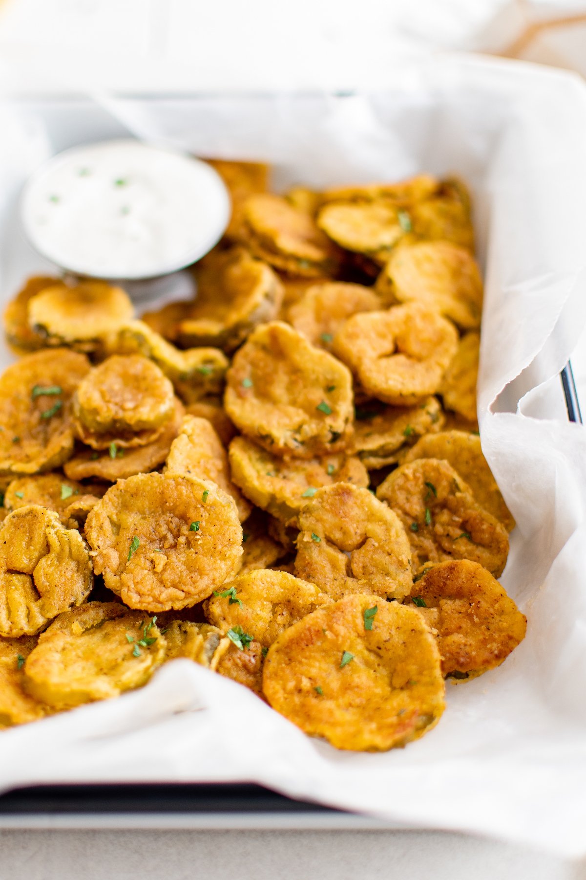 Air fryer fried pickles in a paper-lined dish with ranch sauce.