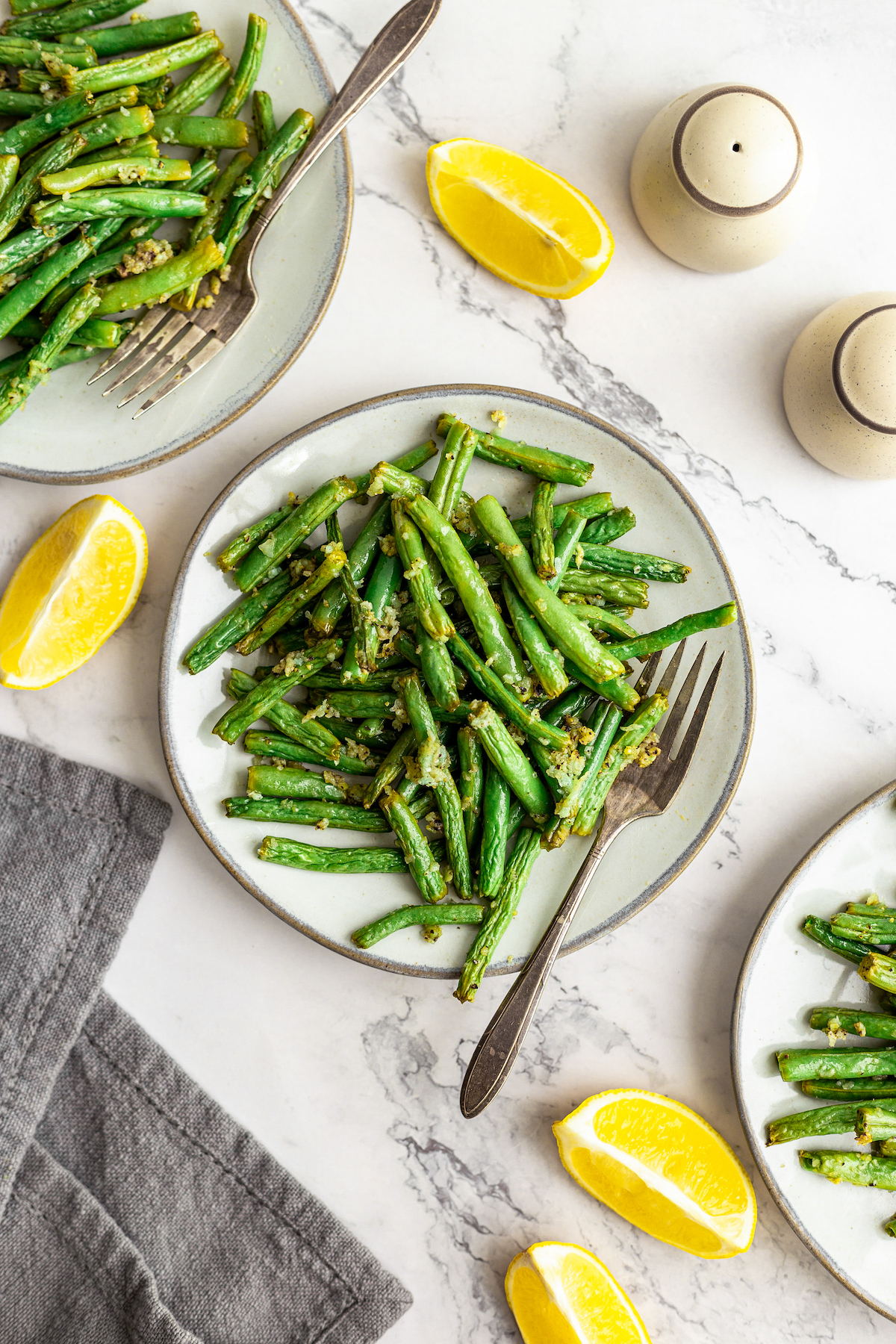 Overhead shot of green beans on dinner plates, with lemon wedges.