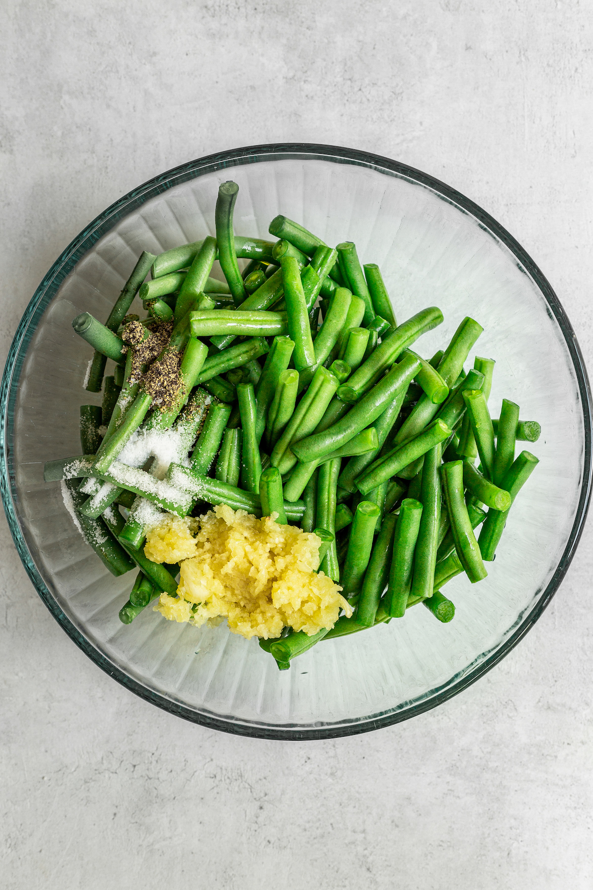 Green beans, garlic, and other ingredients in a glass mixing bowl.