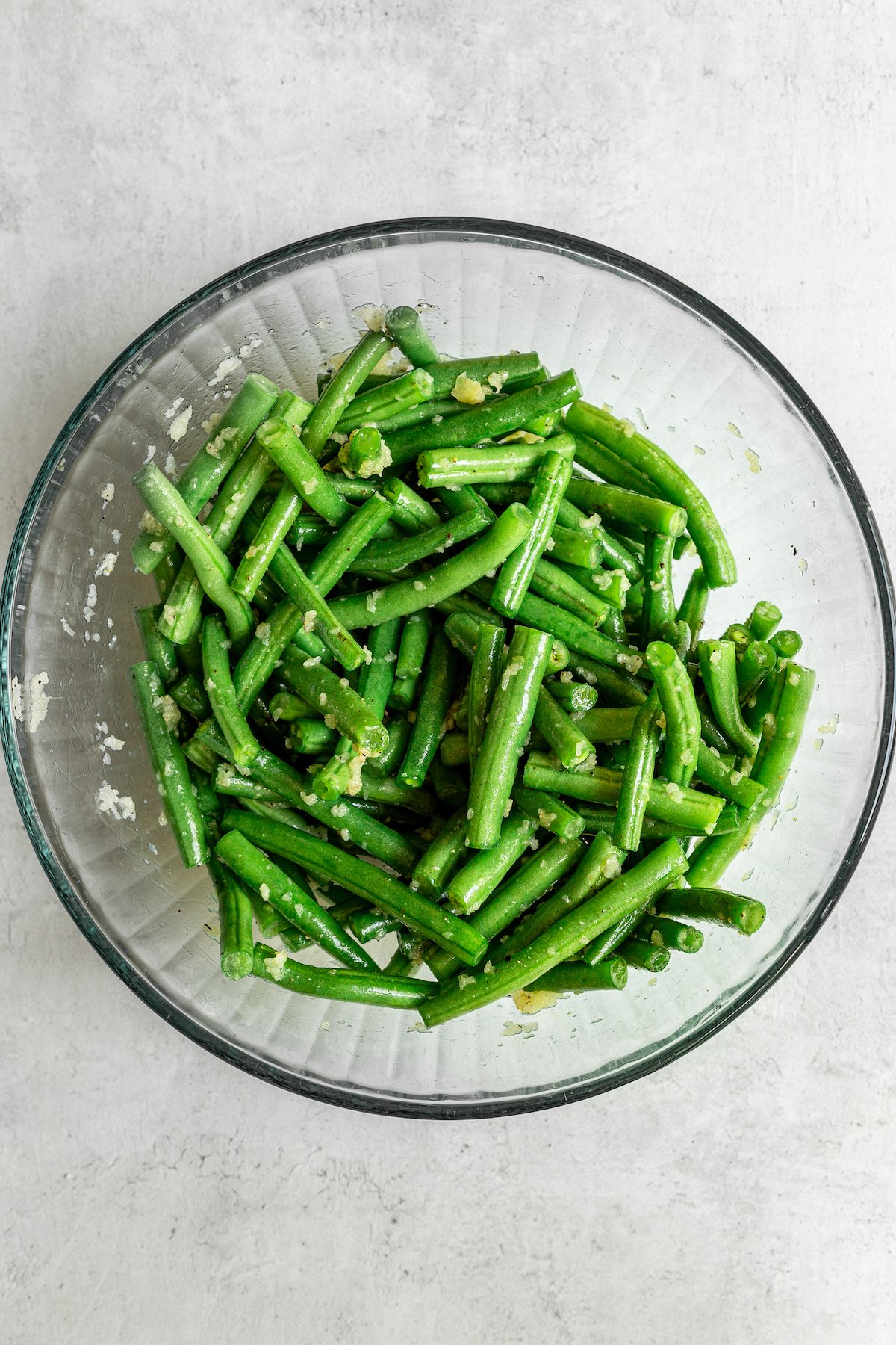 Seasoned raw green beans in a glass mixing bowl.