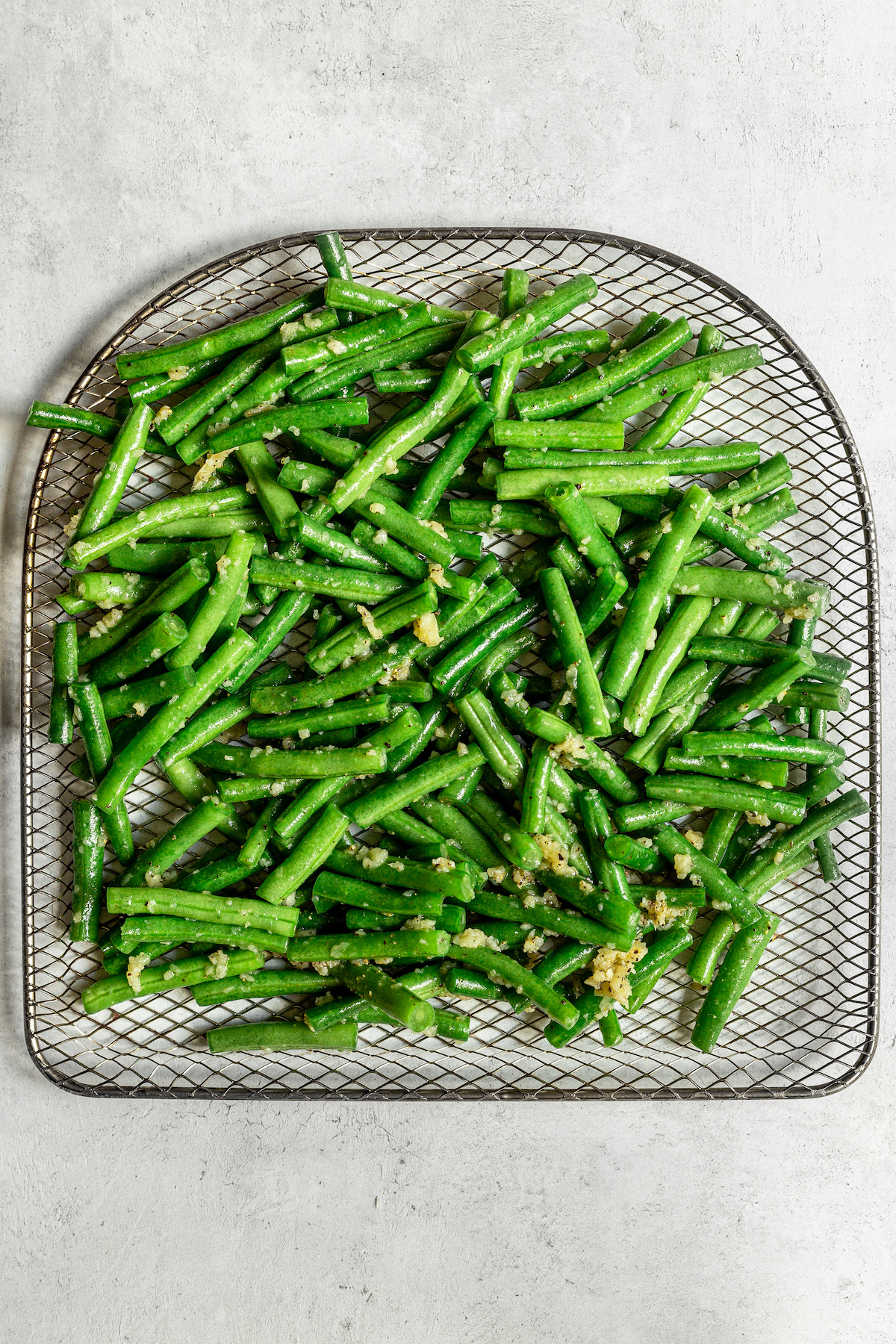 Raw green beans on the tray of an air fryer.