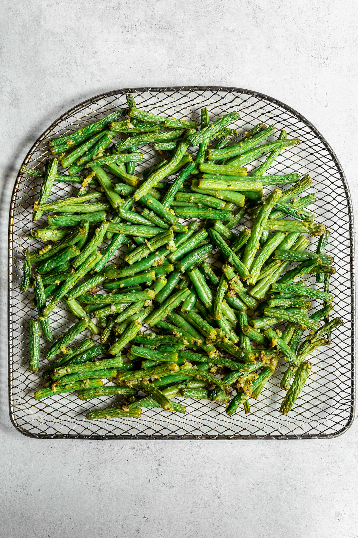 Air-fried green beans on the tray of an air fryer.