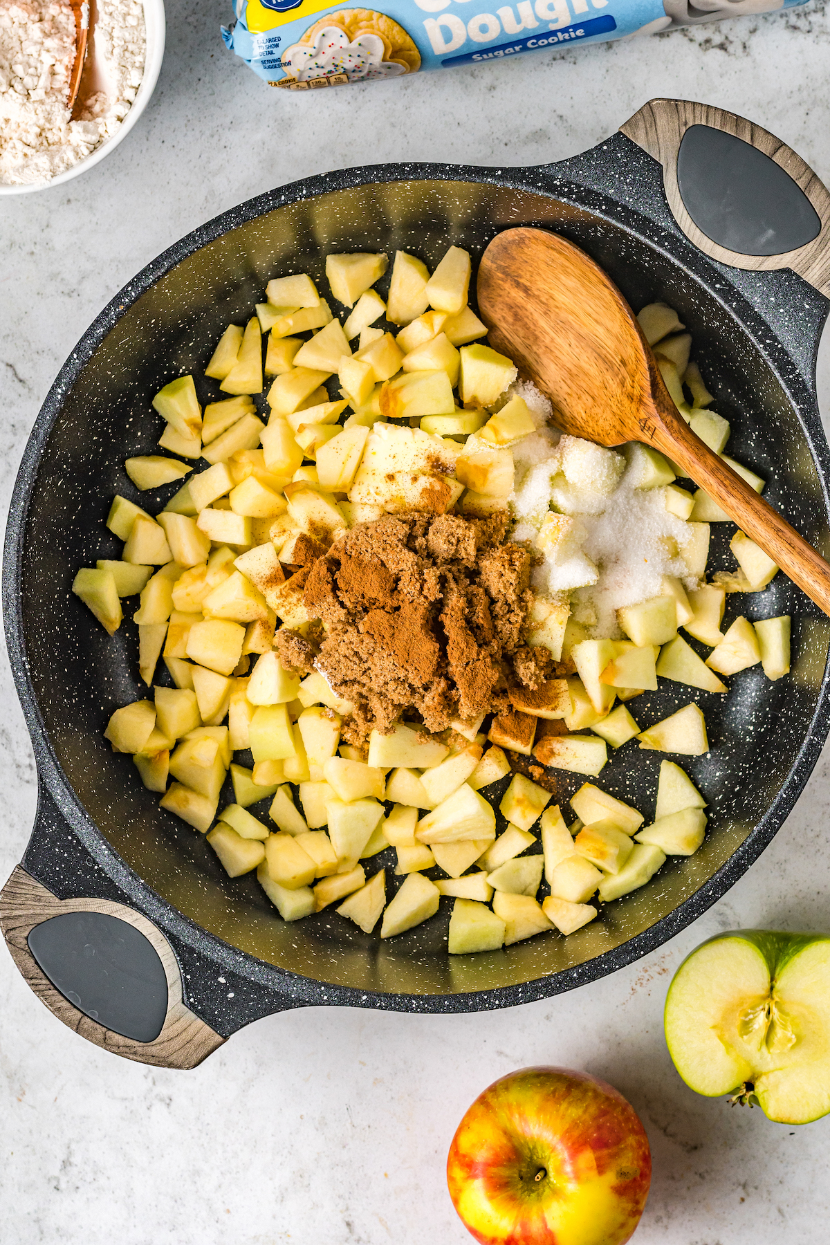 Apples, spices, flour, and other ingredients cooking in a saucepan.