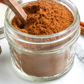 A wooden spoon in a bowl of apple pie spice seasonings.