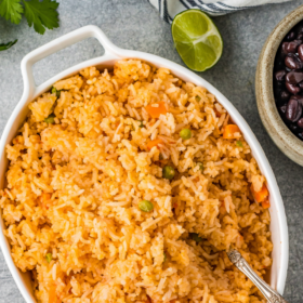 Homemade mexican rice in a white serving dish with a serving spoon.