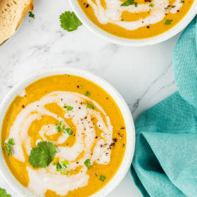Two bowls of butternut squash soup with cream drizzled in it.