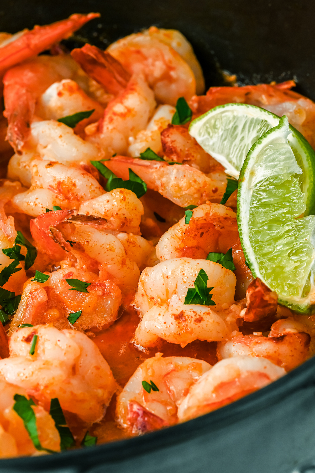A close up of shrimp cooking in a pot, with a parsley garnish and two slices of lime