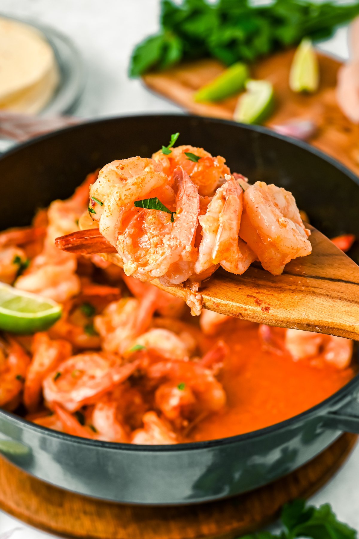 A wooden spoon serving shrimp out of a pot of Camarones al Mojo de Ajo