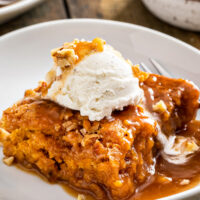 A square of pumpkin cobbler on a white plate, topped with vanilla ice cream.