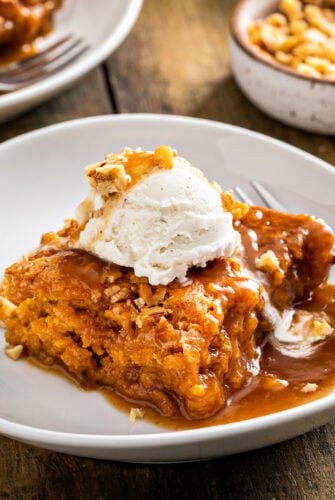 A square of pumpkin cobbler on a white plate, topped with vanilla ice cream.