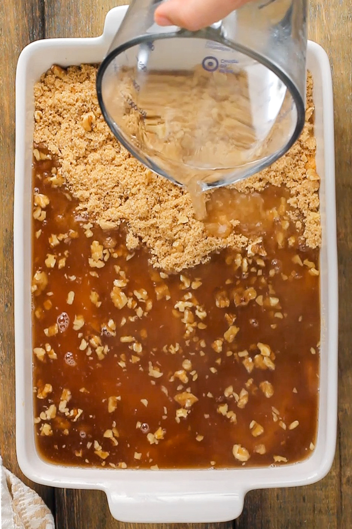 Hot water being poured into a casserole with brown sugar and pecans.