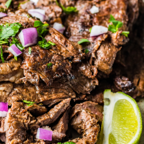 Sliced carne asada on a plate with onion and cilantro with a lime wedge on the side.