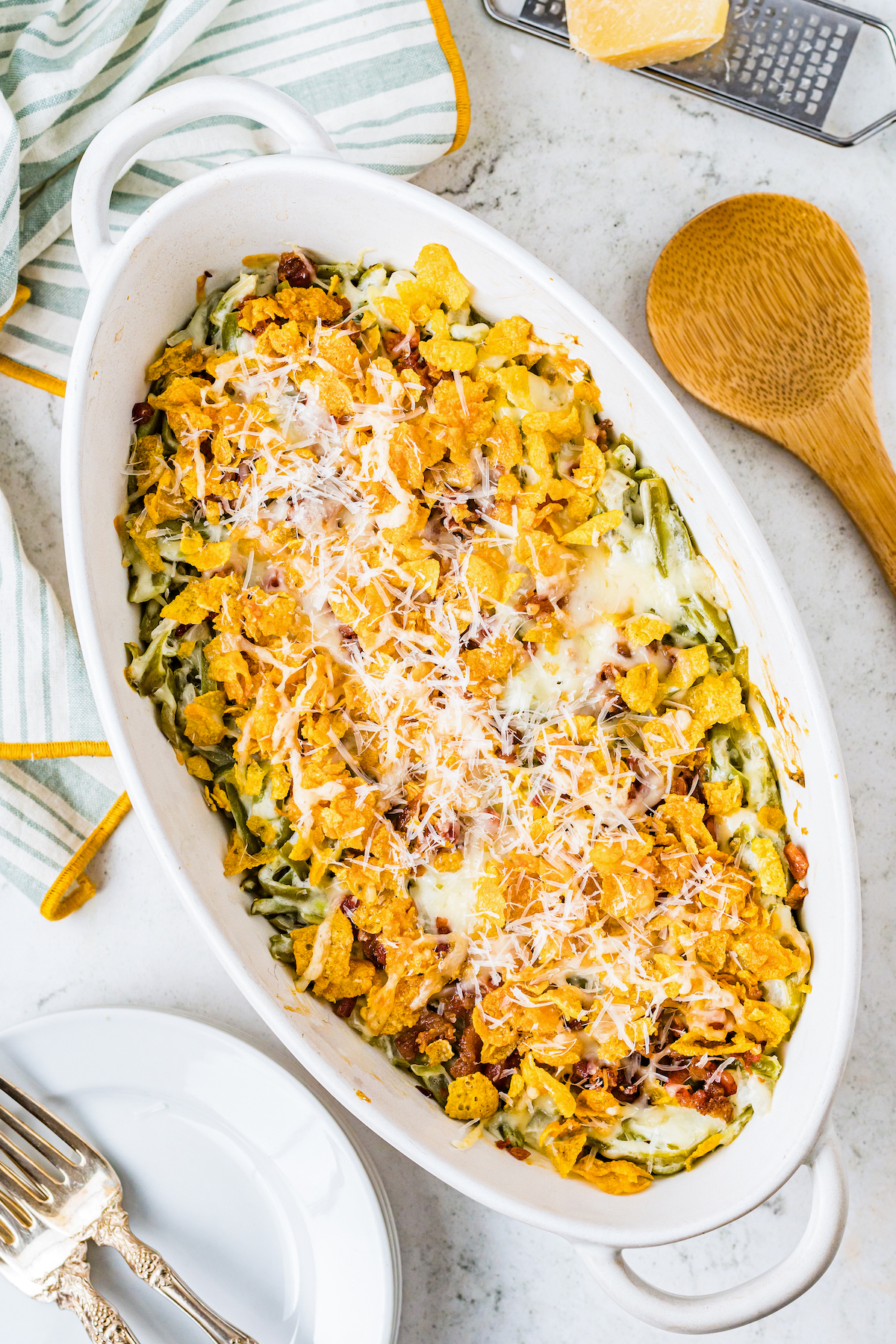An oval casserole dish with a green bean casserole in it, topped with cornflakes and Parmesan.