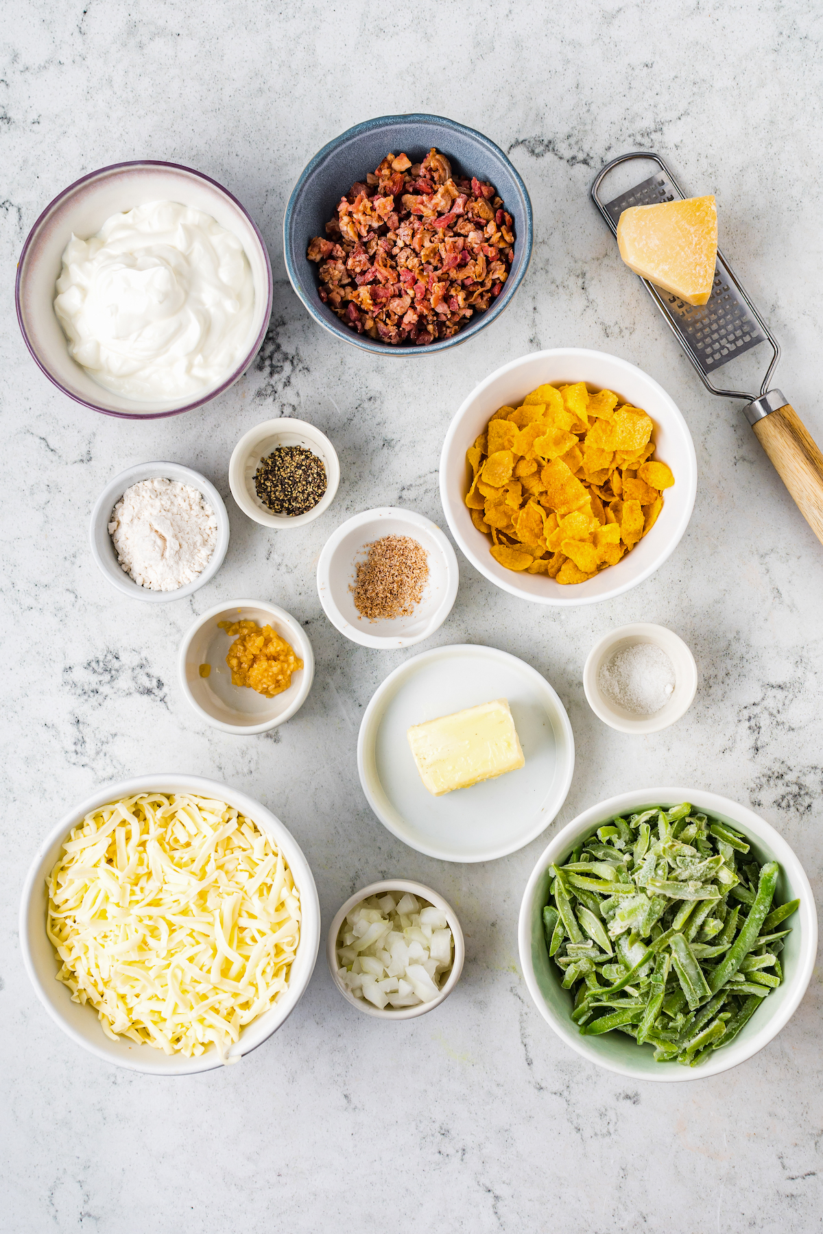 From top left: Sour cream, bacon bits, Parmesan cheese, flour, pepper, nutmeg, cornflakes, garlic, butter, salt, shredded cheese, diced onion, frozen green beans.
