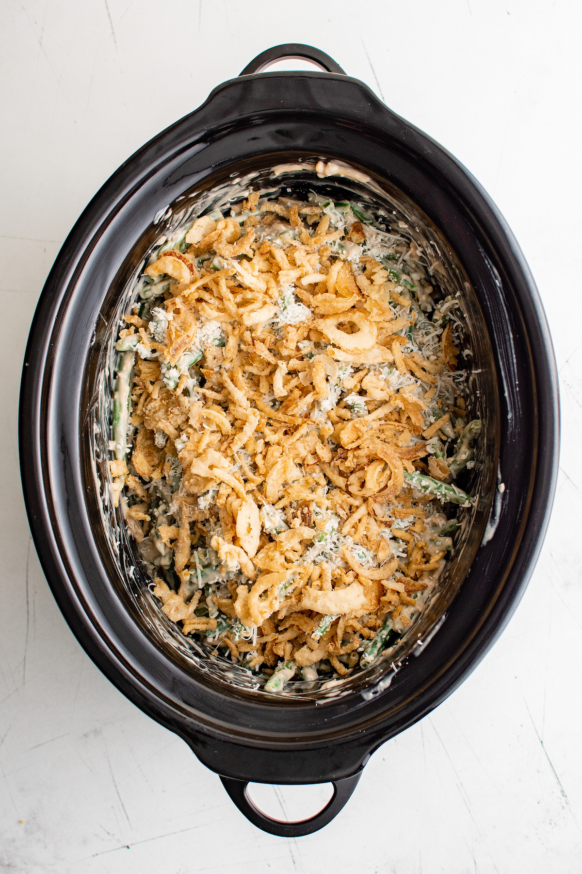 An un-cooked casserole topped with fried onions in a crock pot.