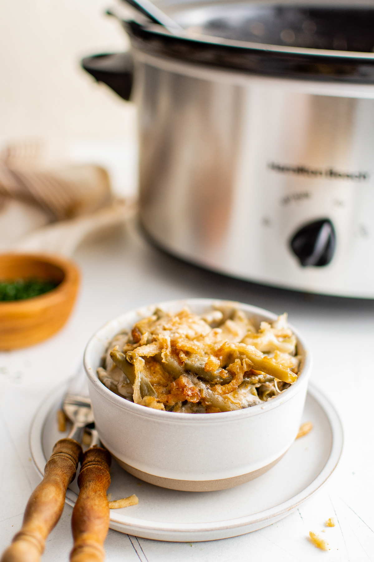 A serving of green bean casserole in a small bowl, next to a slow cooker.