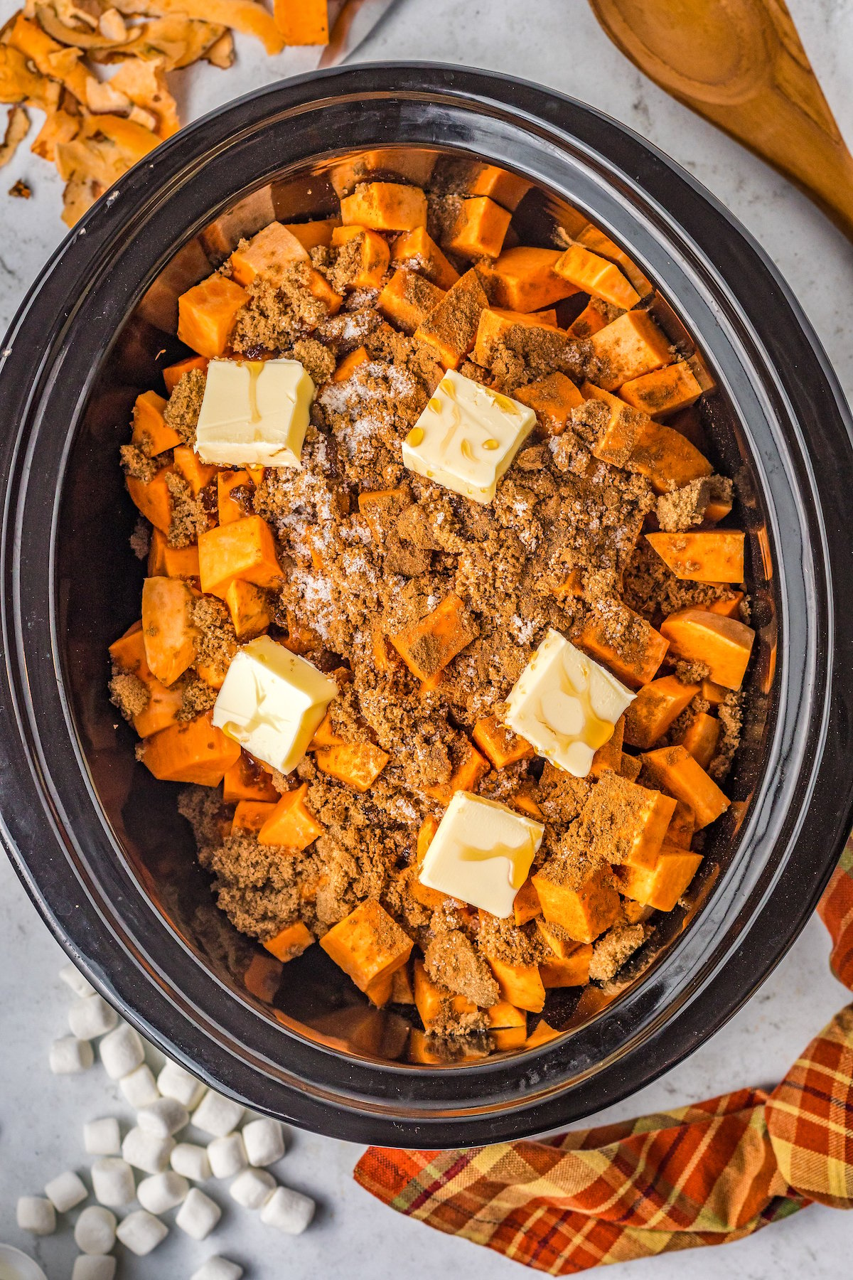 Sweet potatoes in a crockpot with butter, maple syrup, brown sugar and more sprinkled on top of the sweet potatoes.