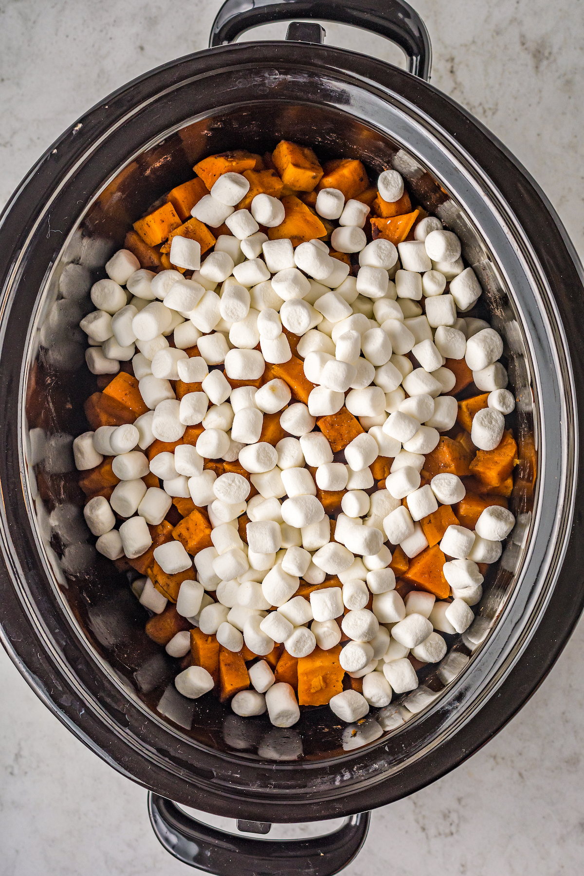 Marshmallows sprinkled on top of cooked sweet potatoes in a crockpot.